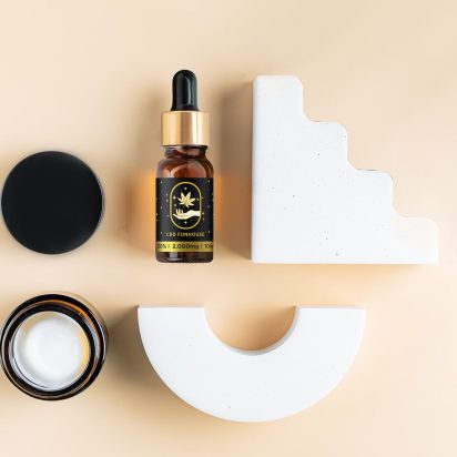 Ulei CBD și recipient cremă cosmetică așezate printre forme geometrice albe.