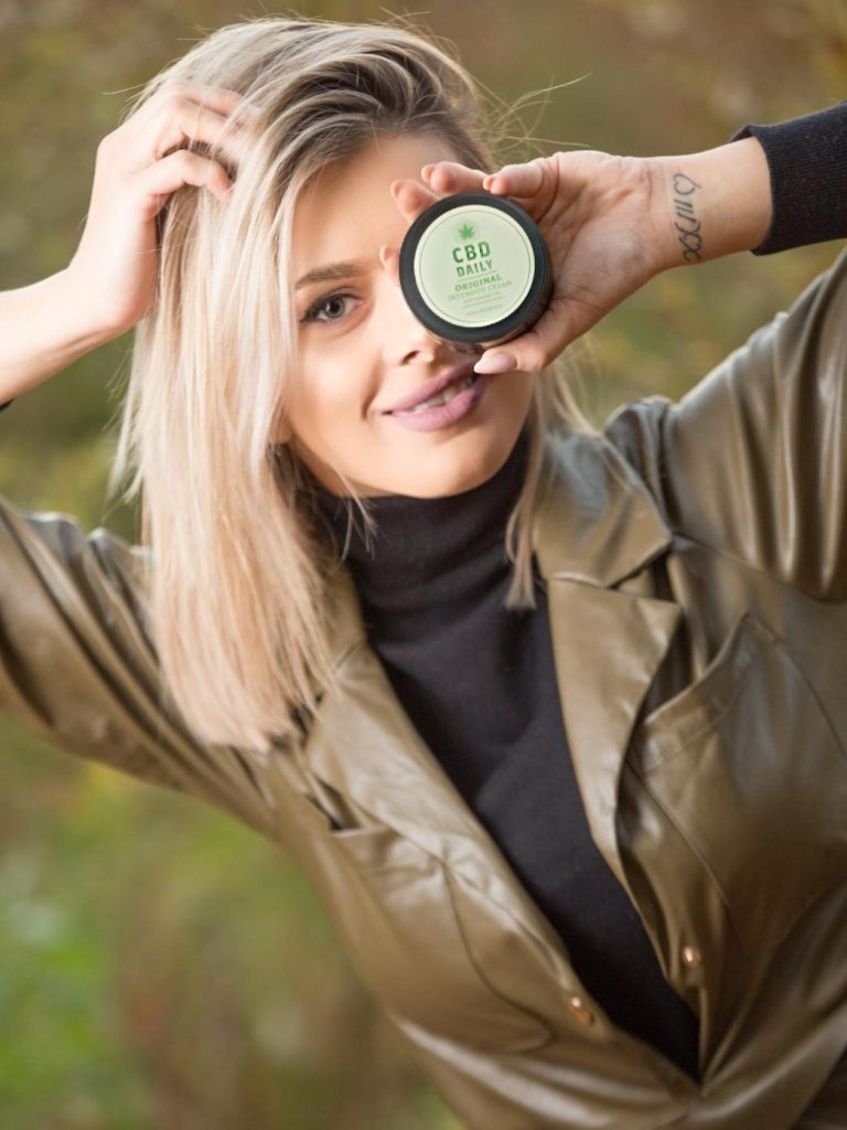 Femeie zâmbind și prezentând crema hidratantă cu efect intensiv CBD Daily.