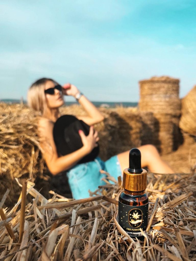 Femeie relaxându-se pe un balot de paie, ținând sticluța de ulei CBD deschisă.