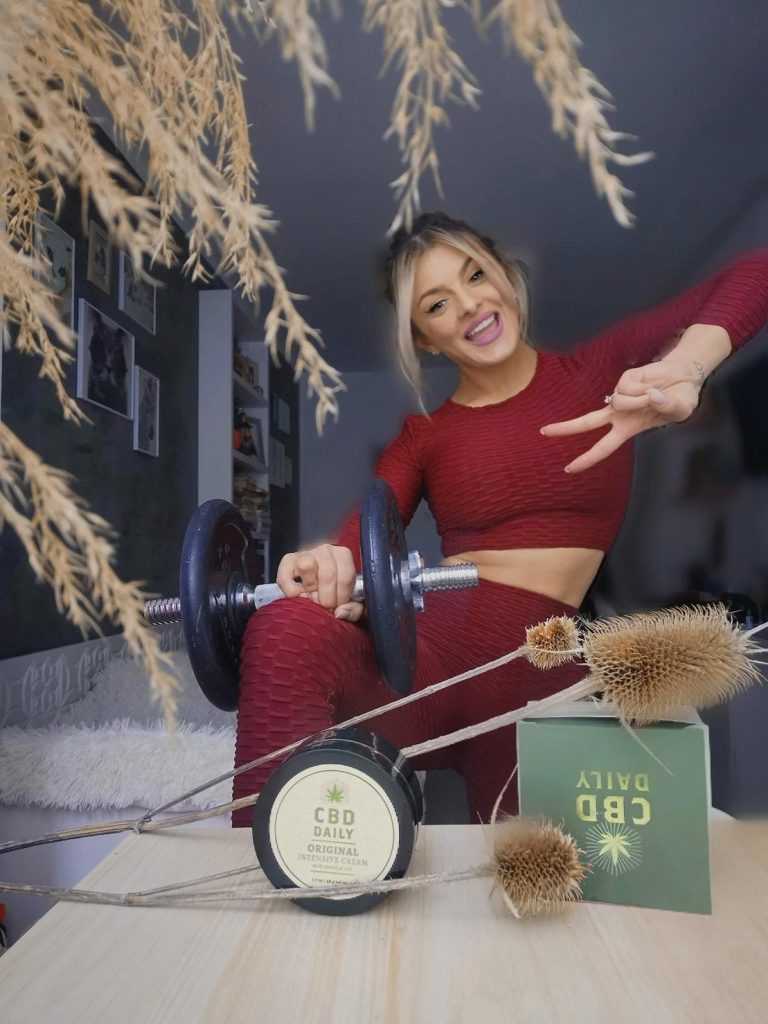 Femeie la antrenament fitness cu greutăți, folosind crema CBD pentru recuperare musculară.
