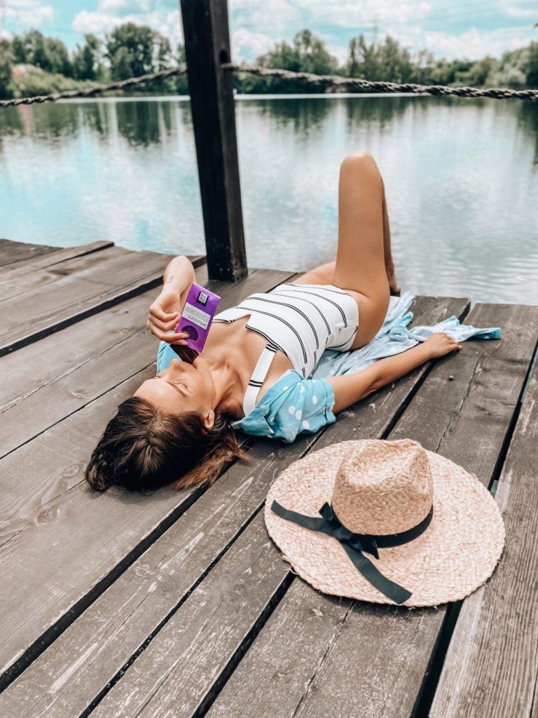 Femeie relaxându-se la soare pe un ponton de lemn, susținând un stil de viață fără stres.