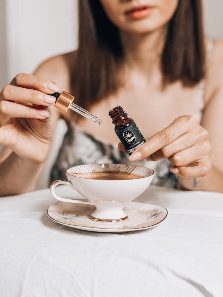 Femeie adăugând picături de extract de canabidiol în ceașca de ceai fierbinte.