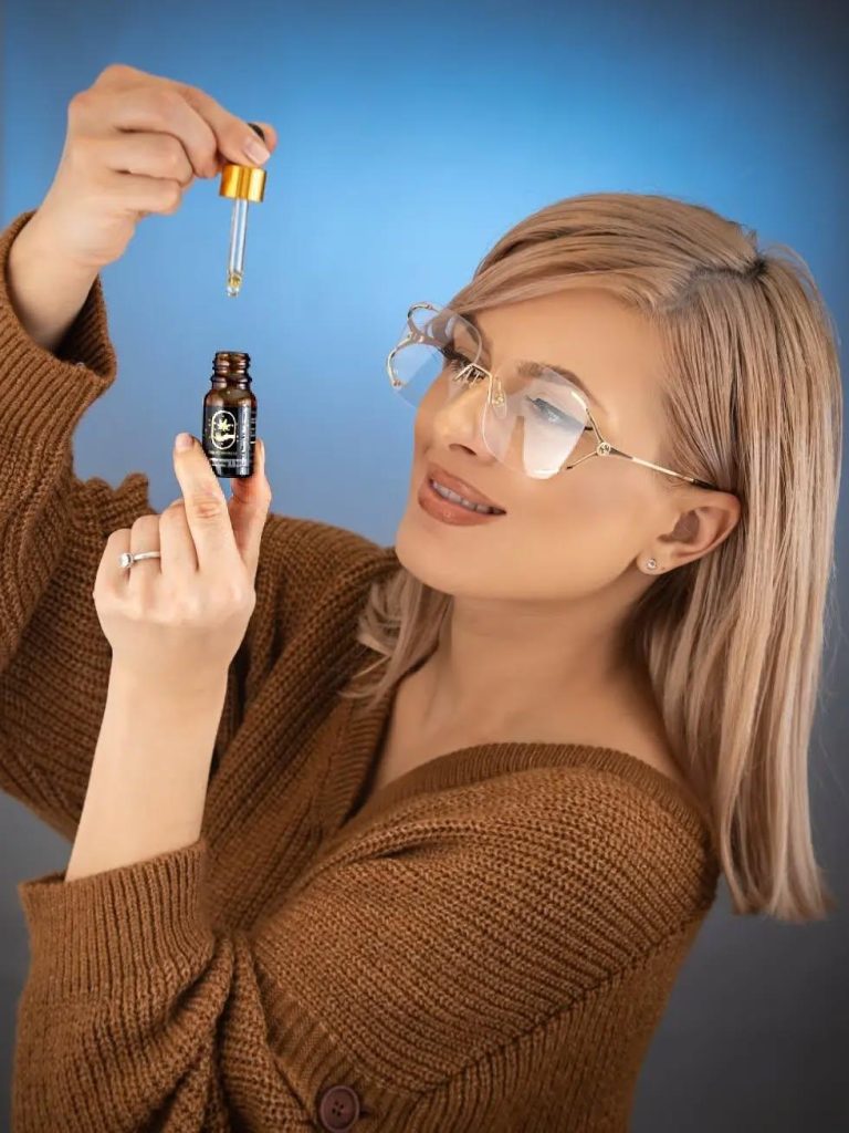Utilizatoare de CBD aplicând picături din extractul de cânepă cu o pipetă din sticlă.