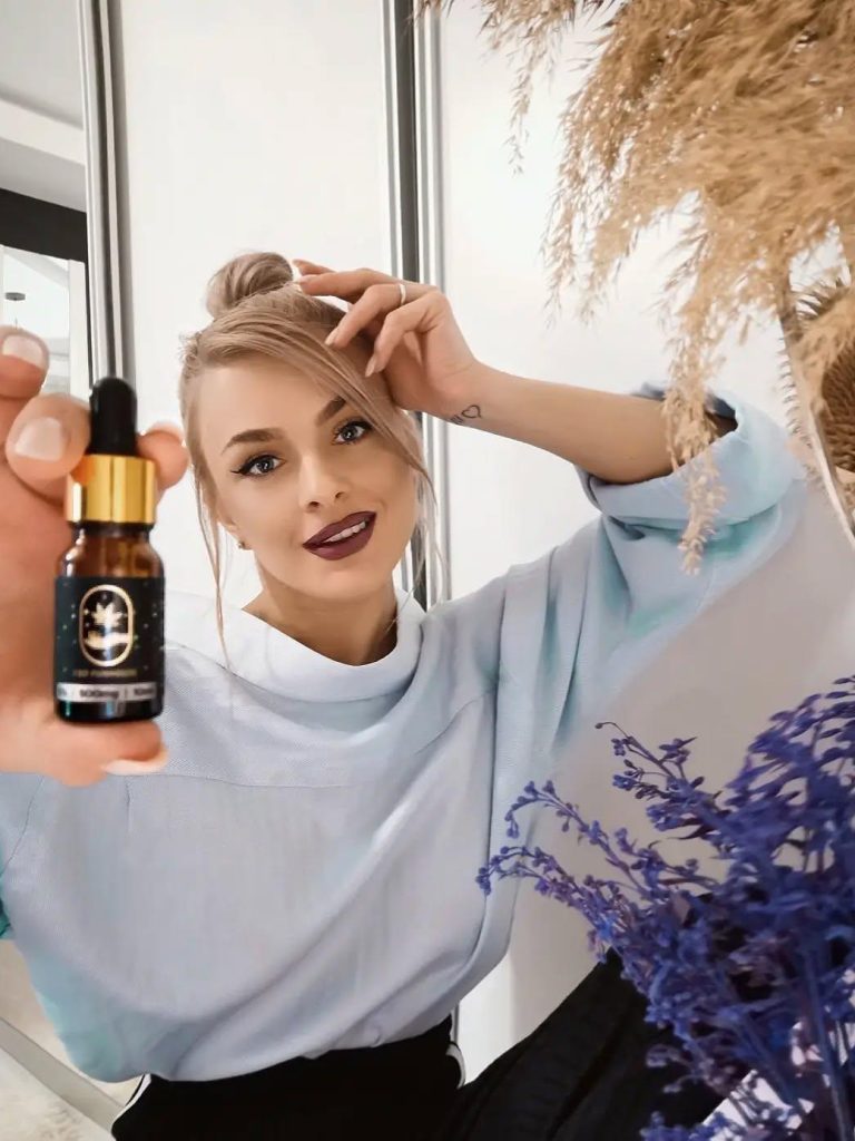 Femeie tânără prezentând zâmbind sticluța de ulei CBD Funhouse premium.